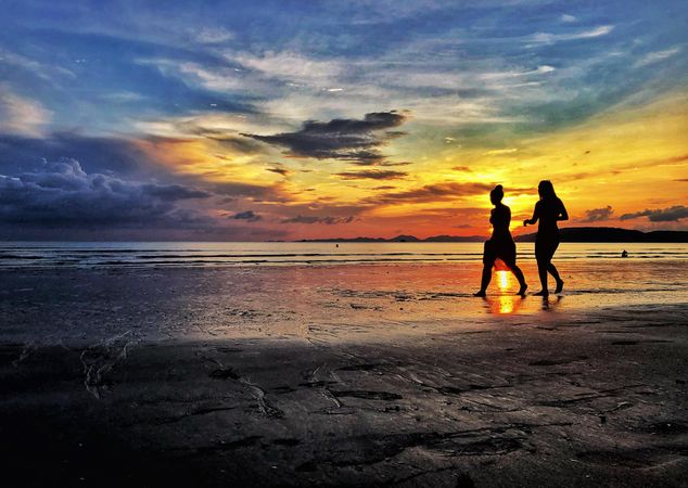 Silhouette of two women walking on sandy beach at sunset in Tambon Ao Nang, Chang Wat Krabi, Thailand