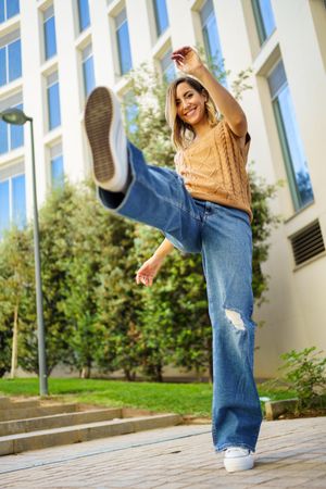 Woman in jeans and vest kicking leg up outside