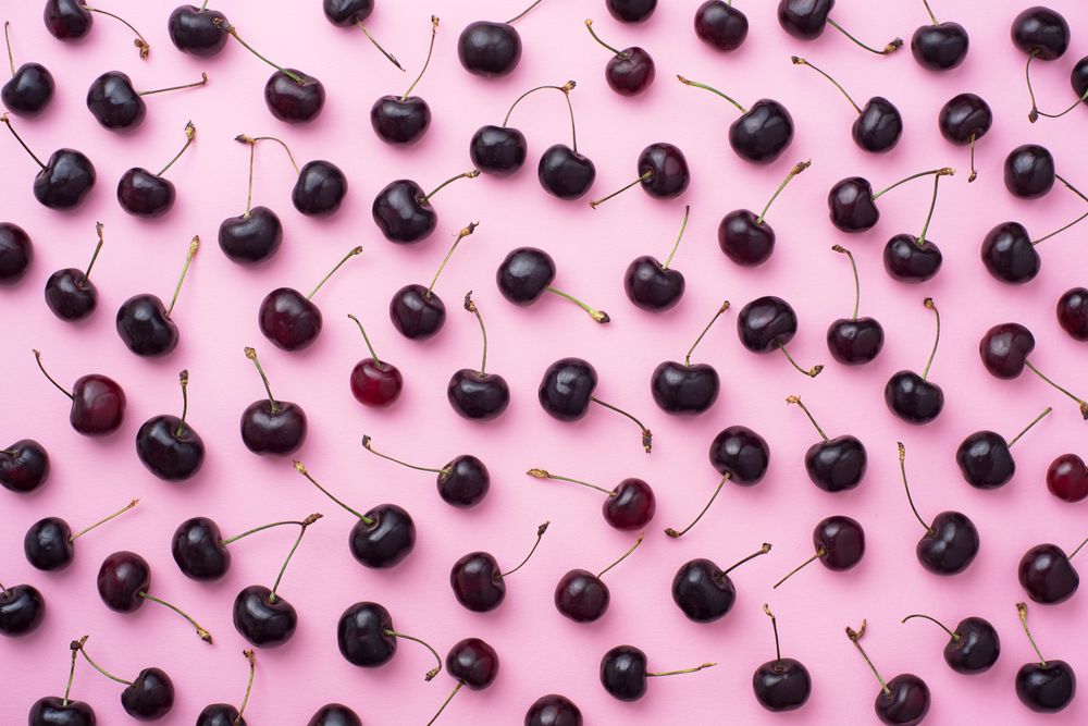 Many cherries scattered over a pink background