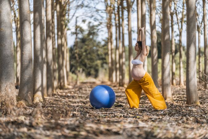 Adult pregnant woman training with pilates ball in park during sunny day