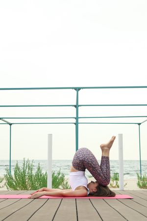Young woman on yoga mat on wooden floor outdoors