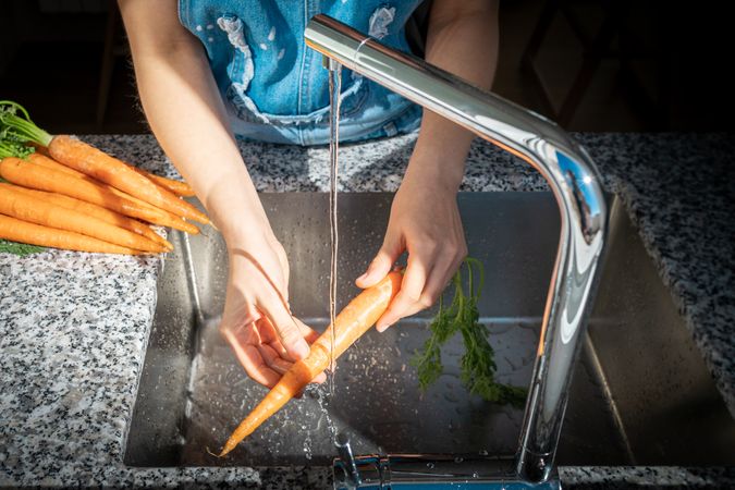 Crop woman hands washing carrot