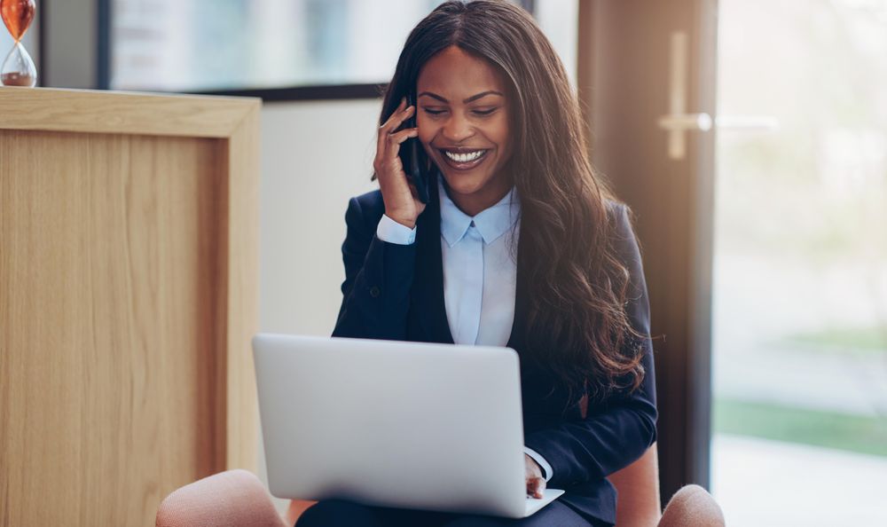 Woman smiling on a cellphone at a laptop