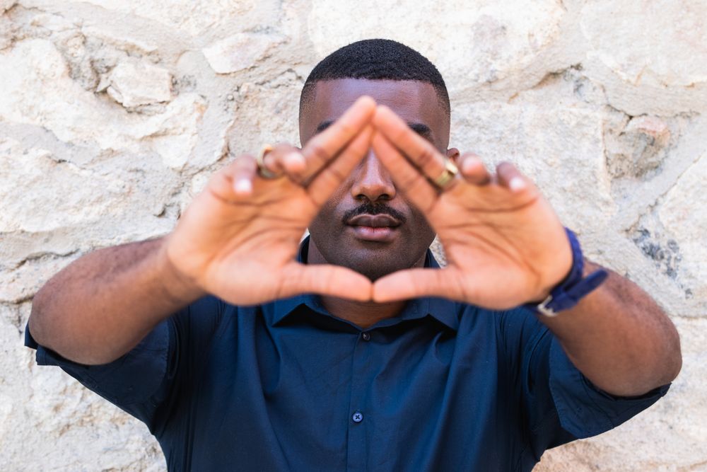 Black man demonstrating triangle gesture with hands near fence