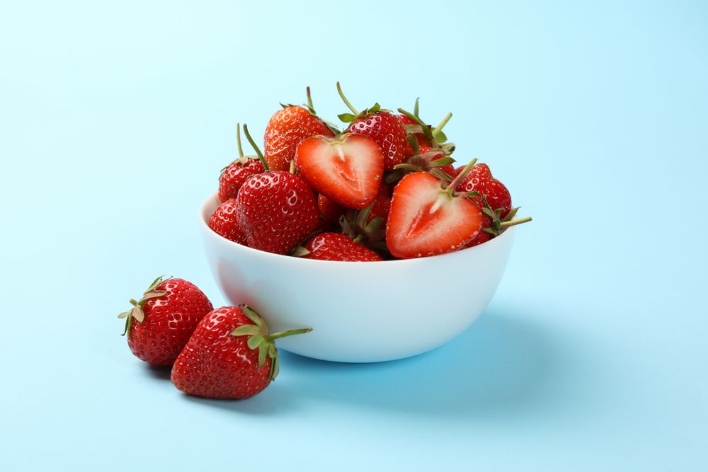 Bowl with tasty strawberry on blue background. Summer berry