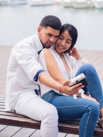 Woman with man taking photo selfie and sitting on bench