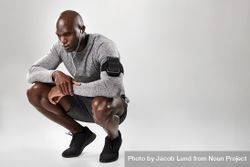 Young African male model with armband and earphone crouching down bEN210