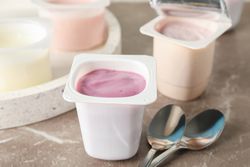 Composition with plastic cups with yogurt on grey table, space for text