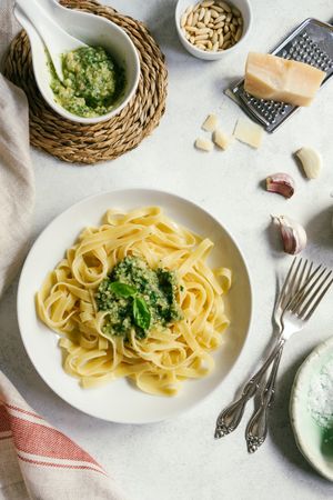 Served plate of pesto pasta next to bowl of sauce on table