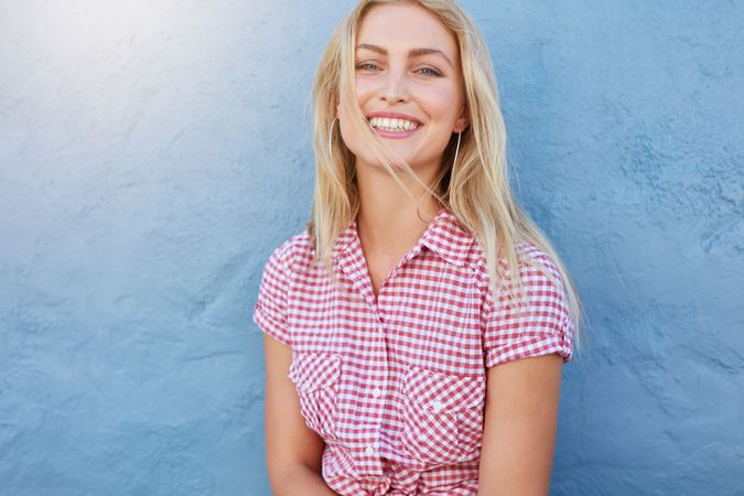 Portrait of cheerful young woman looking at camera and smiling against blue wall