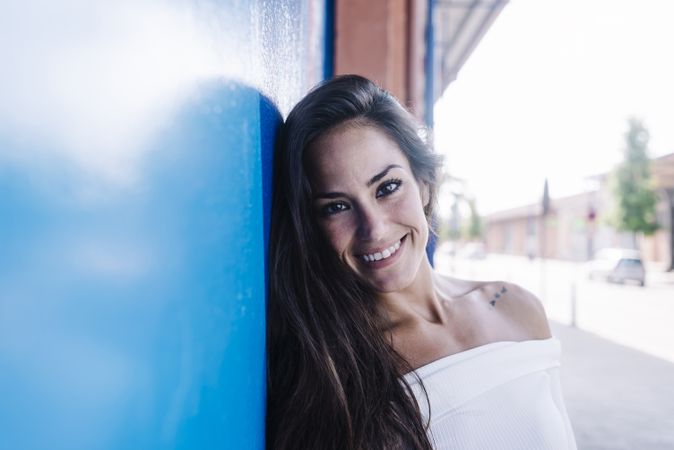 A young smiling woman leaning against a blue wall looking at camera