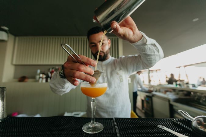 Barman pouring cocktail and alcoholic drinks from shaker in a bar.