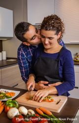 Man kisses wife as she chops vegetables in kitchen 0LlvV0