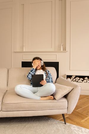 Teen girl humorously covering face while using tablet indoors.