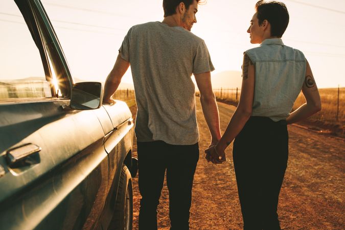 Rear view of couple holding hands and standing on dirt road