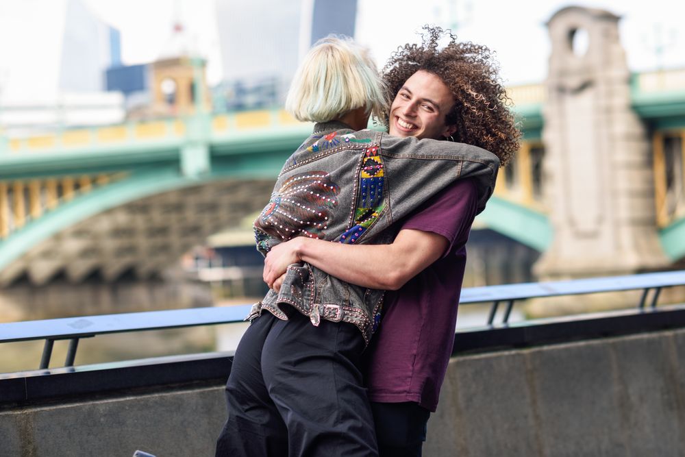 Man lifting up his girlfriend on riverwalk with bridge in background