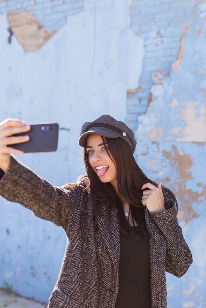 Charming Hispanic woman taking selfie near wall