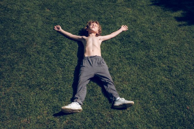 Shirtless boy relaxing on green lawn