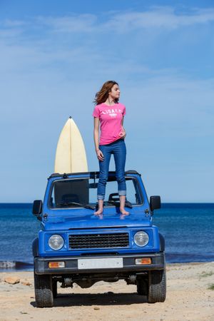 Woman with surfboard standing on top of car