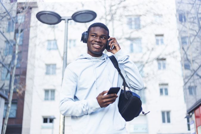Smiling Black man walking in the street while listening music on headphones