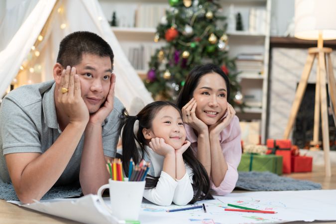 Happy Asian family with chin on hand pose, lying on floor with cozy tent