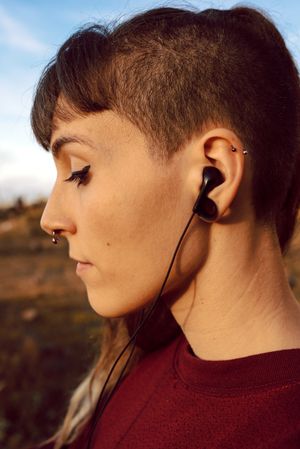 Young woman with piercing listening music on smartphone on hill