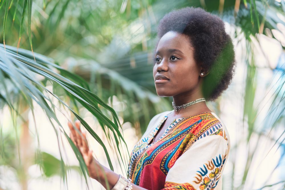 Cheerful Black woman  amidst palm leaves