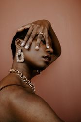 Woman wearing gold necklace and gold ring and gold earring against brown background