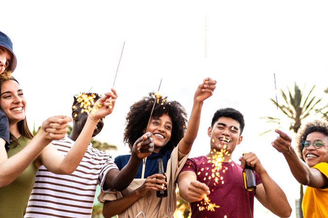 Happy multi-ethnic friends and with sparklers and beer outside