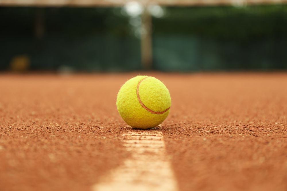 Light green tennis ball on clay court, close up