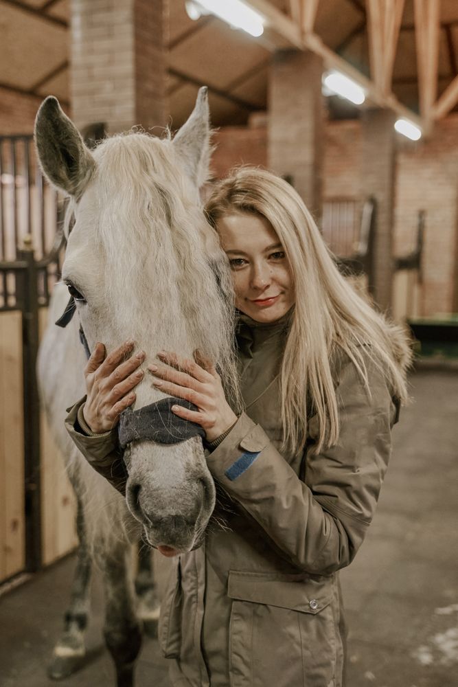 Woman hugging horse with long mane in face in stable