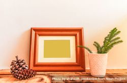 Wooden picture frame leaning against wall with branch and pinecone in vase mockup 0gZJNb