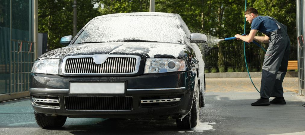 A man washes a car in a manual car wash. Clear car