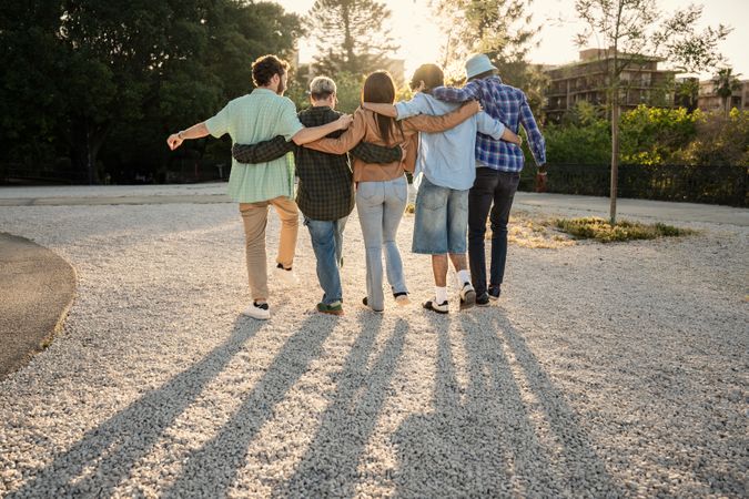 Diverse group of friends walking together on a path towards the sunset.