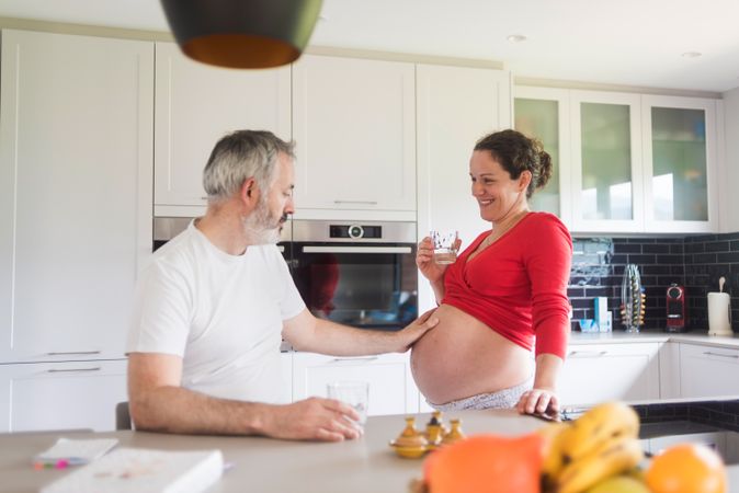 Pregnant woman with husband touching her stomach in kitchen