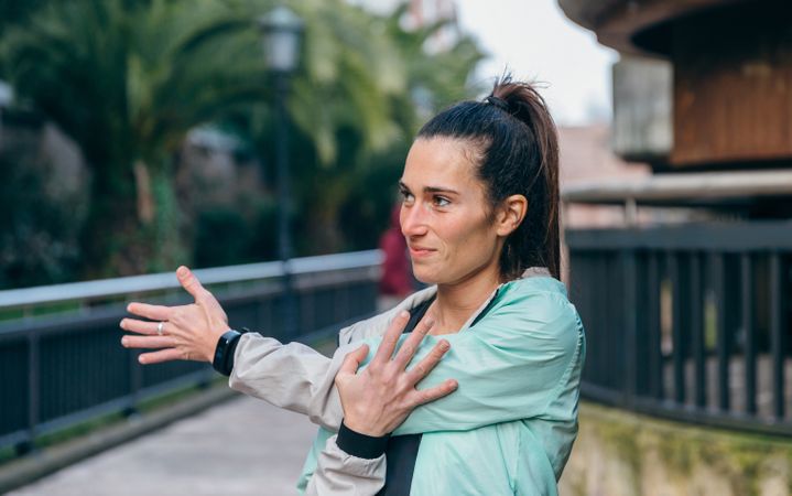 Brunette female runner stretching her arm before training outside