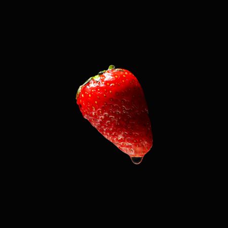 Side view square of water on dark background with a floating strawberry
