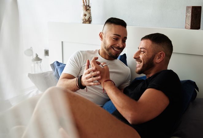 Smiling gay couple hugging on bed