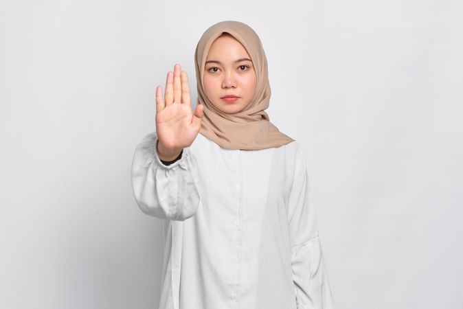 Stern Asian female in headscarf with hand up to stop