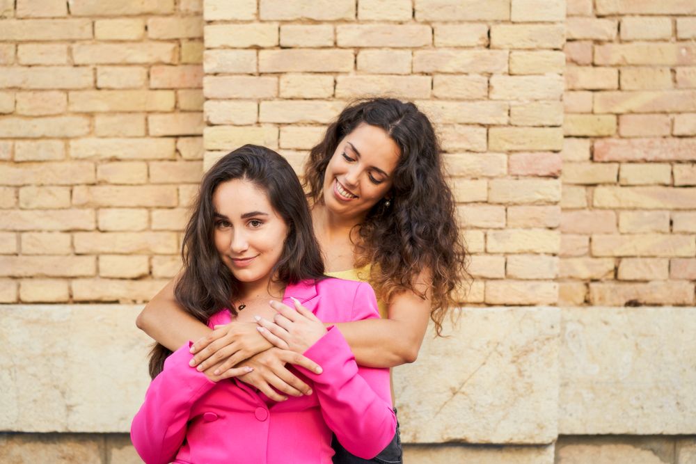 two young women friends embrace each other smiling with joy