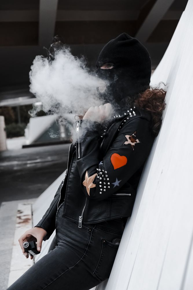 Woman in mask and jacket smoking on street