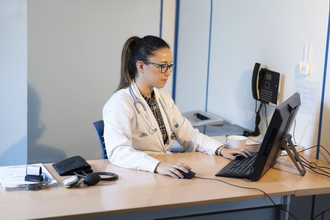Young doctor using computer at table near pulsometer