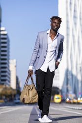 Black man wearing elegant suit walking in the middle of the street while looking into the distance on sunny day