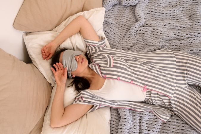Woman smiling playfully while holding pillows on knit blanket.