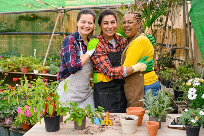 Satisfied diverse gardeners hugging in greenhouse with plants