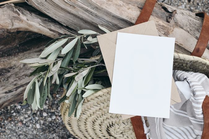 Blank greeting card invitation mockup in straw bag with olive tree branches and towel