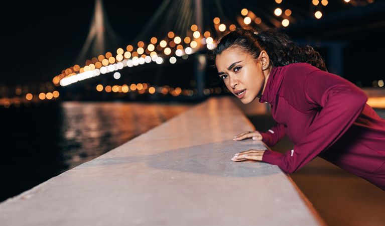 Woman in dark red sportswear doing upper body workout in the evening