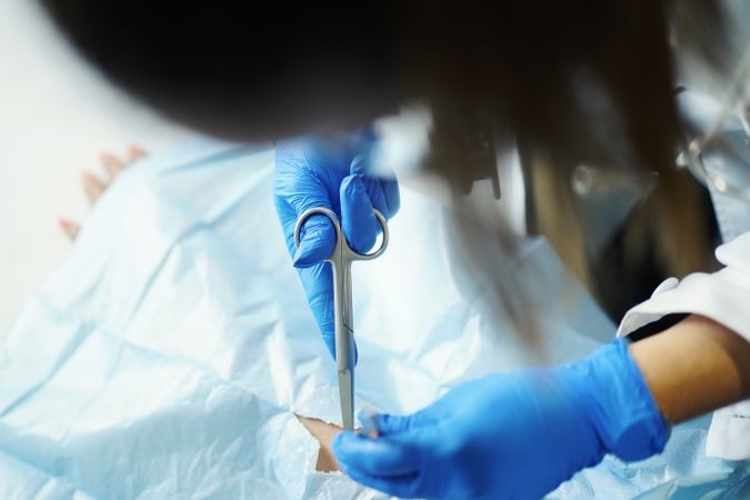 Young doctor with scissors and tweezers near hand of patient