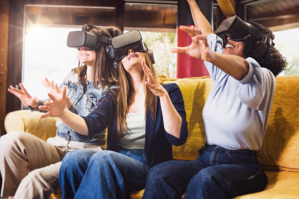 Three women in VR headsets on yellow sofa