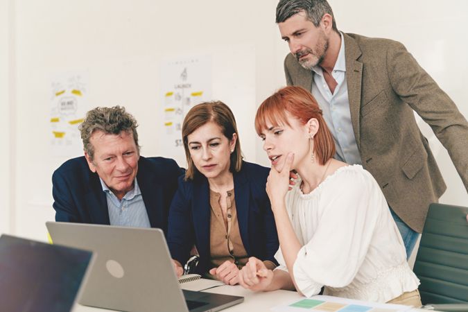 A diverse group of four colleagues gather around a laptop, studying a project together with focused expressions